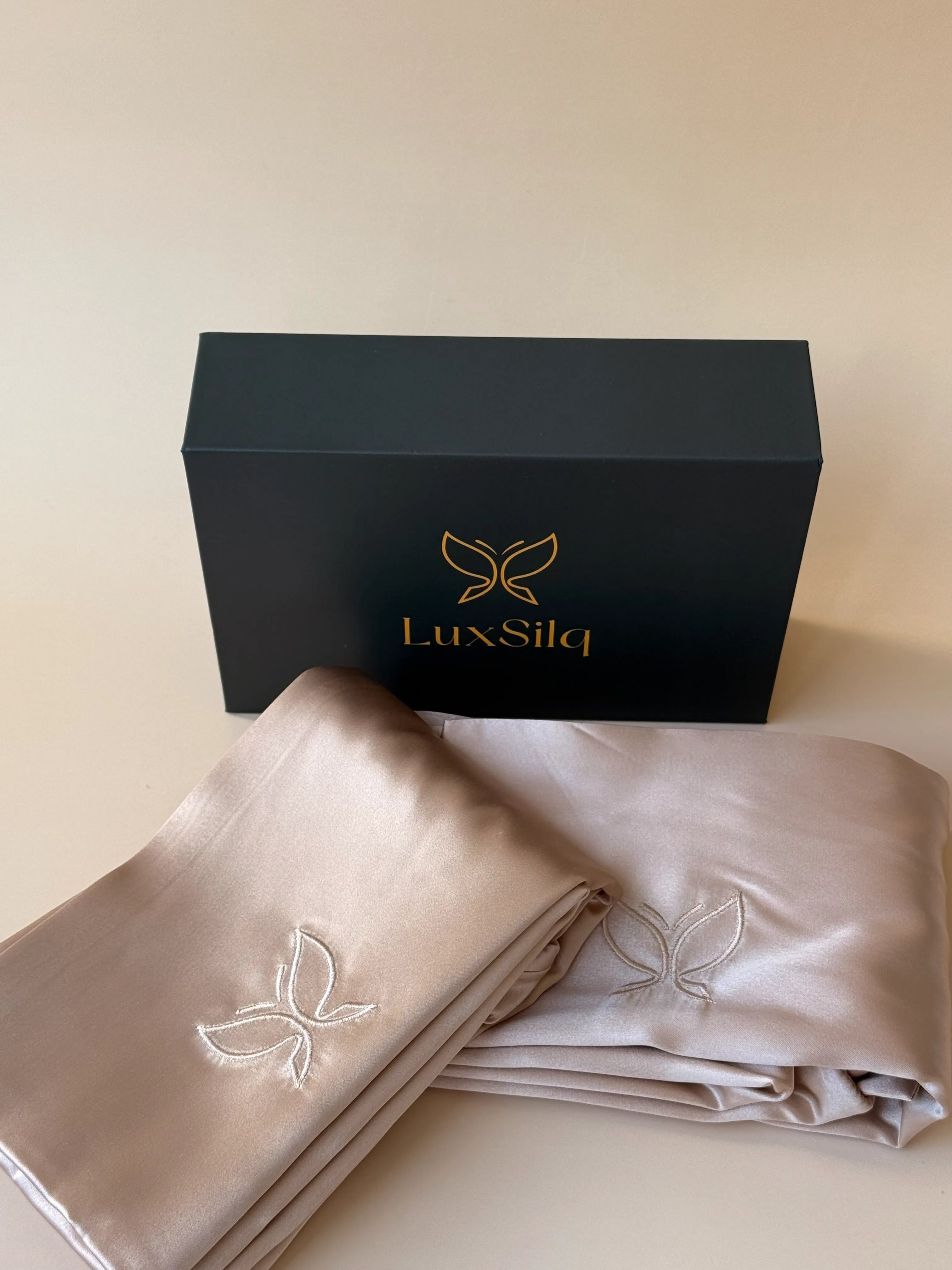 Folded beige satin fabric with embroidered butterfly design next to a black 'LuxSilq' box on a light background
golden sand