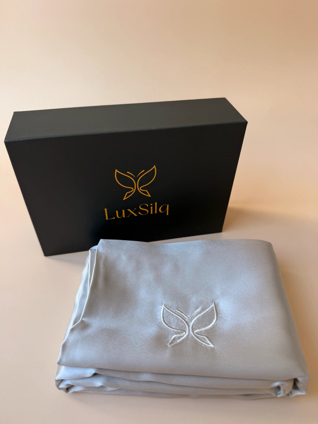 Folded satin sheet with LuxSilq logo next to a black box with the same logo on a beige background
moonlight